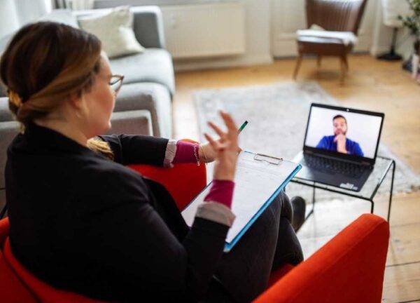 A woman is talking with a man virtually over a laptop.